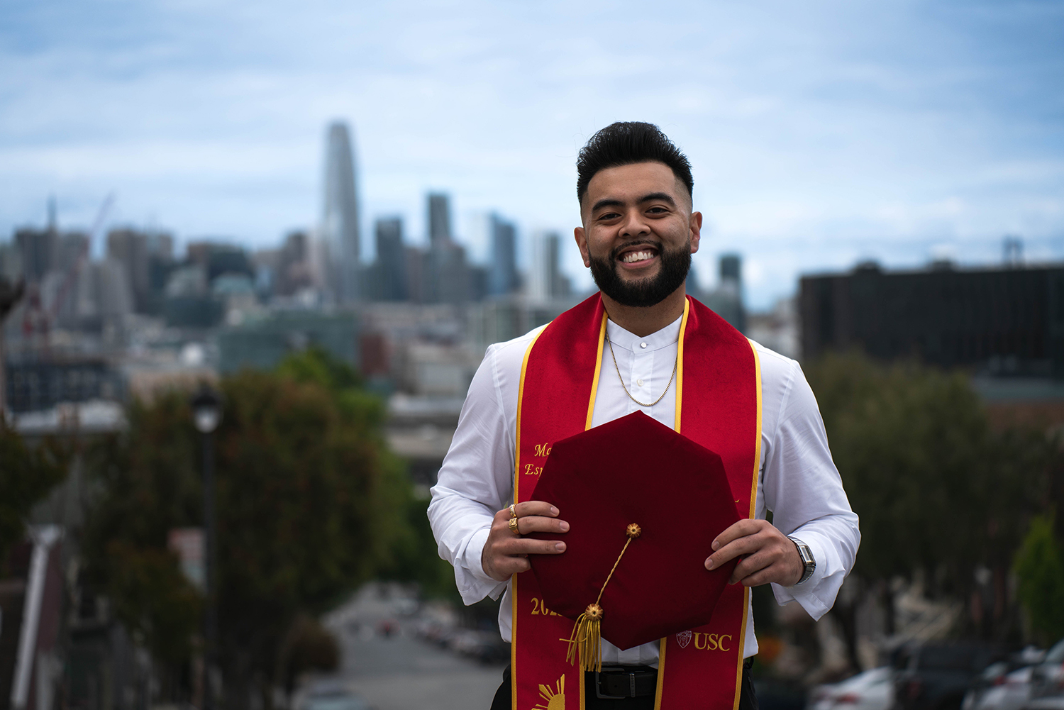 Matt Espanol in Commencement regalia with the city of San Francisco behind him