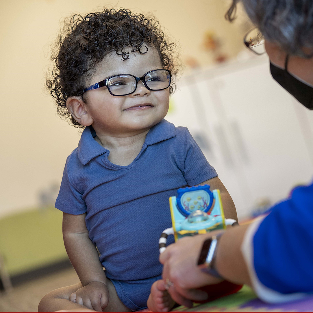 Baby at risk for cerebral palsy with glasses on, working with physical therapist